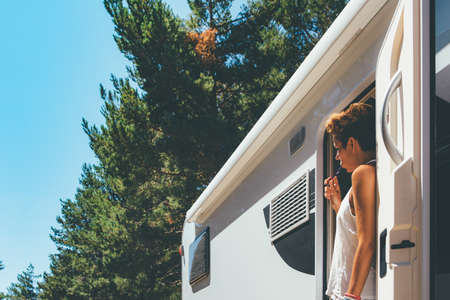 Side view of a young woman is brushing her teeth on a caravan door parked on a forest on a holiday...