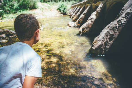 Back view of a young boy admires a river at the nature on a sunny day. Copy space area availableの写真素材