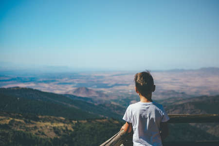 Back view of a young boy admiring the landscape in the mountain on a sunny day. Copy space area availableの写真素材