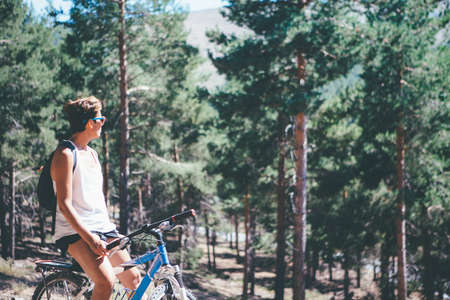 Young sporty woman with bicycle standing looking at the landscape in the woods. Copy space area availableの写真素材