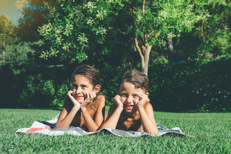 Smiling boy and girl with the hands resting on the chin are lying down on the grass taking a sunbath on a sunny summer day. Copy space area availableの写真素材