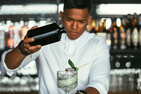 Detail of alcohol poured in a cocktail glass by a mixed race male expert bartender at the bar...