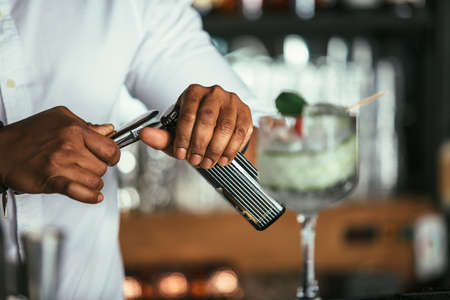 Close up of the hands of a mixed race male expert bartender opening a bottle to prepare a cocktail...