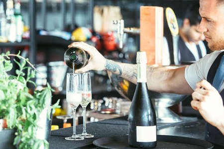 Cropped view of the hands of a tattooed waiter is serving alcohol in a glass ready to serve