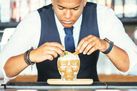 Close up view of a concentrated mixed race male expert bartender is decorating a cocktail with precision at the bar counterの写真素材