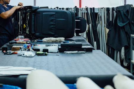 Side view of a cropped view of a man upholstering a car seat in leather on a work table full of tools in a upholstery factoryの写真素材