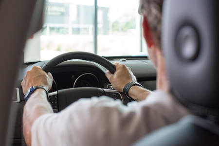 Cropped view of a back view of a man holding a car steering wheel while is drivingの写真素材