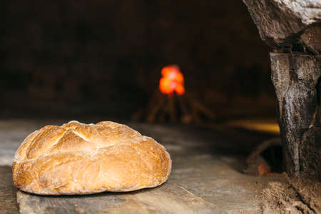 Closeup of a handmade bread in a roman wood burning oven with the fire at the background.