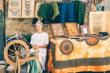 PUERTOMINGALVO, TERUEL, SPAIN - AUGUST 5, 2018: Portrait of a smiling spinner woman in traditional clothes sitting beside her stand in a medieval fair celebrated in Puertomingalvo, a small town located in the Maestrazgo Cultural Park in the region of Gudaのeditorial素材