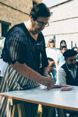 PUERTOMINGALVO, TERUEL, SPAIN - AUGUST 5, 2018: Old woman is making handmade sausage during an...