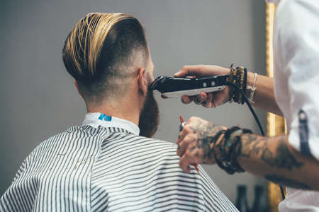 Hipster customer getting trendy beard haircut by a tattooed hairstylist at the barbershopの写真素材