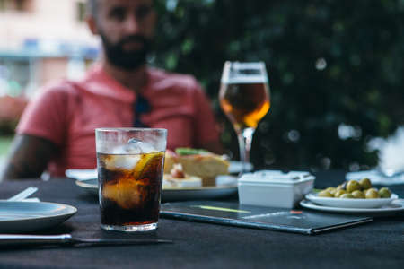 Close up of a fresh  drink glass and a young man tasting spanish tapas and drinking beer at the bar terrace outdoors at the backgroundの写真素材
