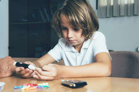 Diabetic child is making a lancing with a puncher in the doctor office. Child diabetes conceptの写真素材