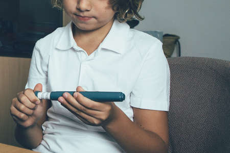 Cropped view of a diabetic child using an insulin pen in the clinic. Child diabetes concept