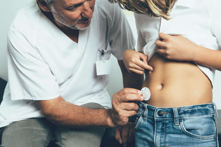 Close up view of a doctor is helping to a young diabetic patient to connect an insulin pump dressing in his abdomen in his office. Child diabetes conceptの写真素材