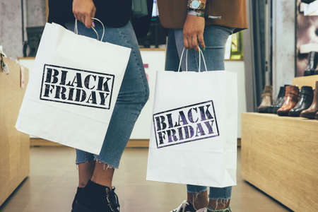 Black Friday. Cropped view of a couple of young female shoppers holding paper shopping bags in a shoe store.の写真素材