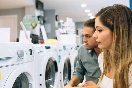 Side view of a young woman and man are looking at the features of a washing machine in a home appliance store. Cyber Monday concept.の写真素材
