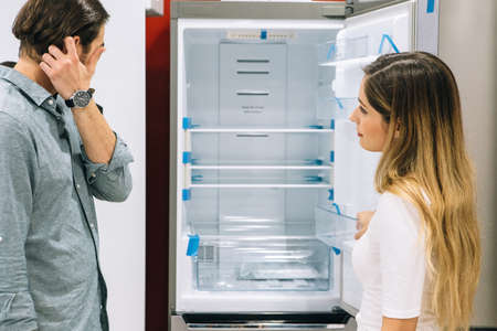 Young woman and man looking at the features of a fridge in a home appliance store. Cyber Monday concept.の写真素材