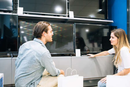 Smiling young couple choosing a television in a home appliance store. Cyber Monday concept.