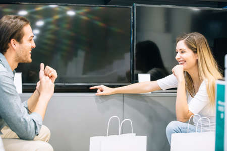Smiling young woman with male friend choosing a television in an appliances store. Cyber Monday concept.の写真素材