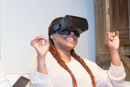 Happy young woman is using virtual reality glasses and she is having fun seated in the sofa at home.