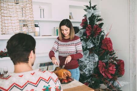 View of a young woman standing is carving a roasted turkey on a Christmas table decorated in front of her beloved manの写真素材
