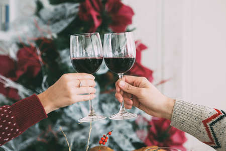 Cropped view of the hands of a woman and a man toasting with wine glasses on Christmas time with a fir tree at the backgroundの写真素材