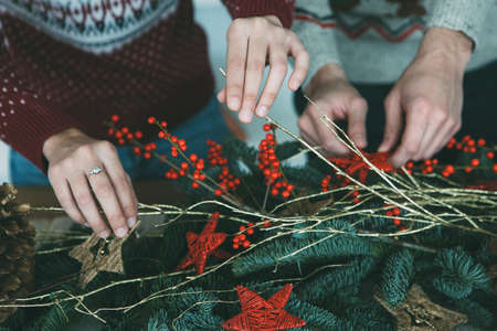 Cropped view of a young woman with a young man are decorating a table with Christmas ornaments wearing Christmas sweatersの写真素材