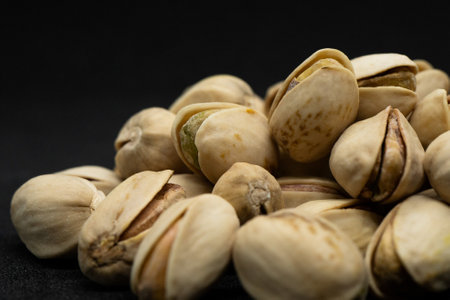 Roasted pistachio nuts in shell on black background (Antep Fistigi), poured roasted peanuts...