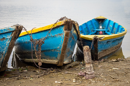 Some rowboats chained to a post on the shore of a lake.の写真素材