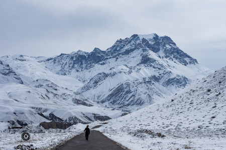 A man walking on a road with the snow covered Himalayan Mountains in the rear.の写真素材