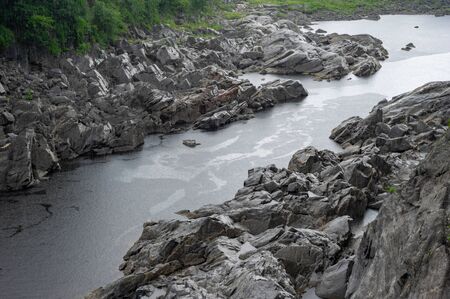 A rocky shoreline along the bank of a river as it is raining.