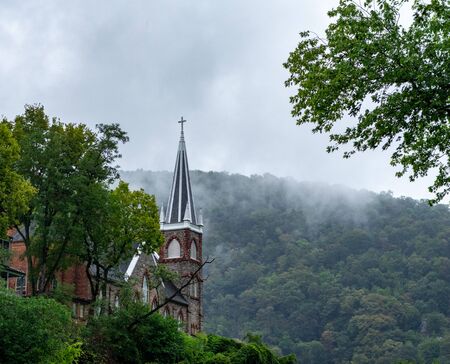 A church steeple poking above the trees on a hillside with fog coming down over the mountains.の写真素材