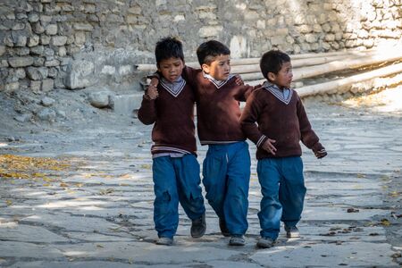 Marpha, Nepal - November 11, 2019: Three schoolboys holding arms and walking down the road to school in Marpha, Nepal.のeditorial素材
