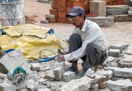 Bhaktapur, Nepal - November 17, 2019: A skilled craftsman using a chisel and a hammer to shape stone for a temple rebuilding project after the earthquake in 2015.のeditorial素材