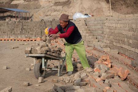 Kathmandu, Nepal - December 31, 2019: A Man Stacking Bricks on a Wheelbarrow at a Brickyard Factory...