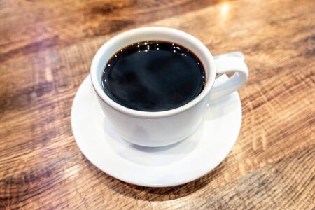A cup and saucer of coffee or kopi sitting on a woodgrain syled table indoors.