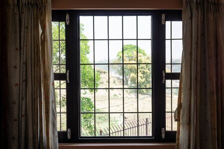 Standing indoors and looking out of a window with bars on it and curtains on the side.