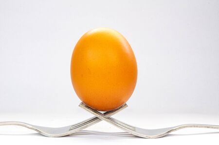 A brown egg sitting on two forks on a white background.の写真素材