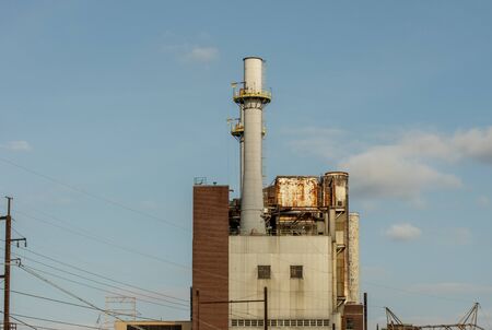 An old building or factory with exhaust stacks pointing up into the blue sky.