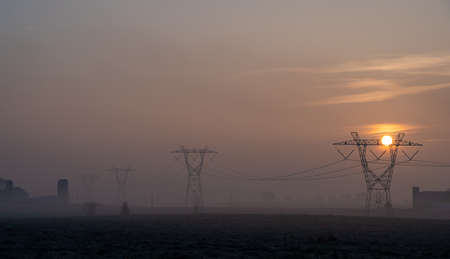 HighHigh Voltage Power Lines running through the countryside in the light of the sunrise.