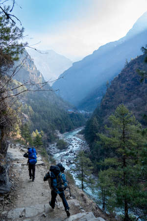 A river in a valley in the Himalayan Mountains of Nepal in the morning light and shadows with some porters on a trail.の写真素材