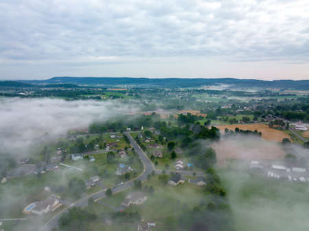 An aerial view from above the fog as it covers the landscape, fields, farms and small towns in the early morning light.の写真素材