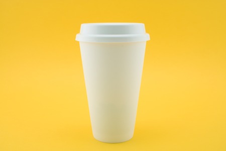 Take-out coffee cup from coffee shop on yellow background. The coffee paper cup is covered with lid.の写真素材