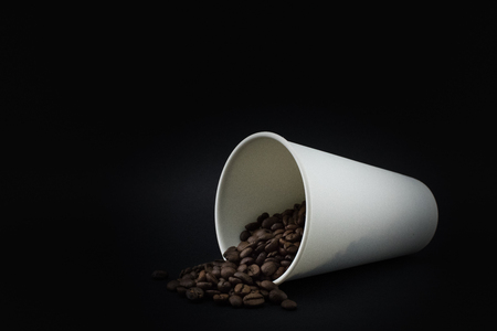 Paper coffee cup with spilled coffee beans, black background. Roasted coffee beans.の写真素材