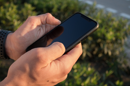 Hands of a young person using his smartphone on the outside. It's the sunset. Person sending a text message and checking social networks.の写真素材