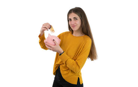 Young woman inserting a banknote into a pig piggy bank isolated on white background. Concept of saving money.の写真素材