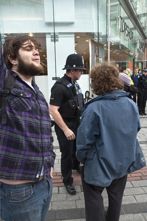 Occupy Exeter activist Bench campaigning out the Exeter branch of Topshop with Devon & Cornwall police officer in the backgroundのeditorial素材