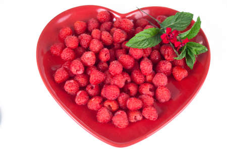 Juicy red raspberries on a red heart shaped plate with a sprig of mint.