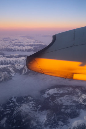 View from the window of a plane flying over the mountains at sunset